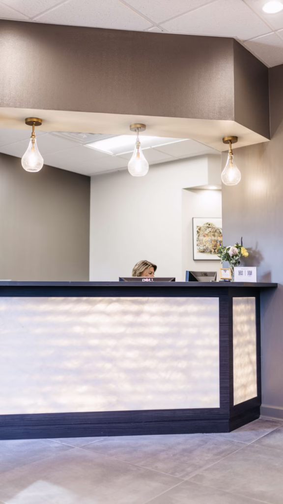 Reception desk in a modern lobby with three hanging pendant bulbs; a person sits behind the counter.