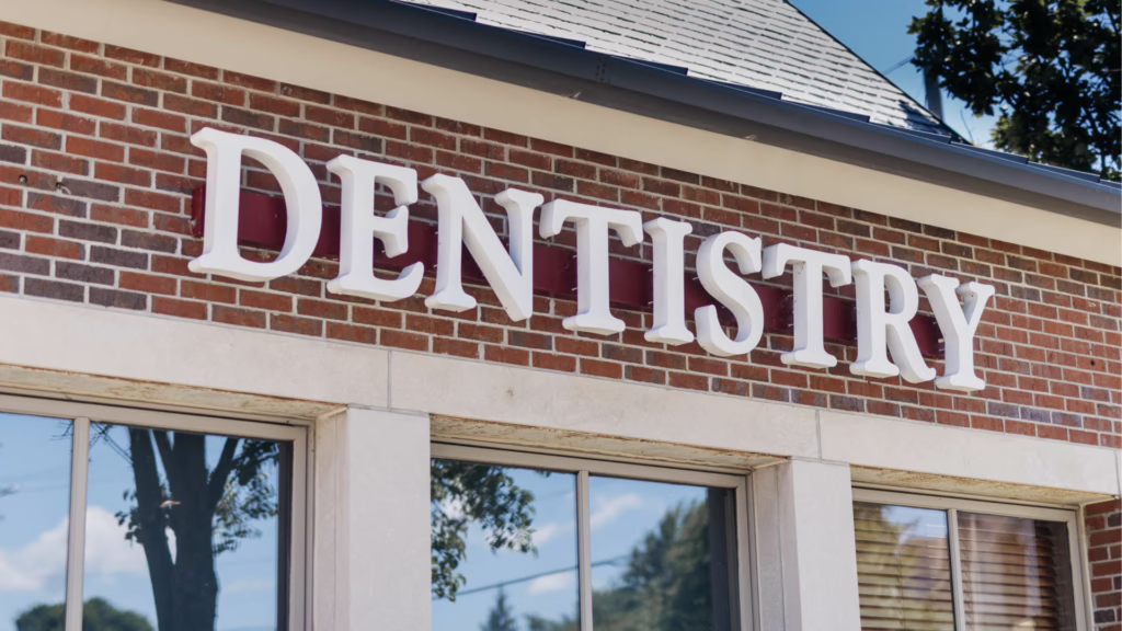 Brick storefront with large white sign spelling DENTISTRY above windows, indicating a dental clinic