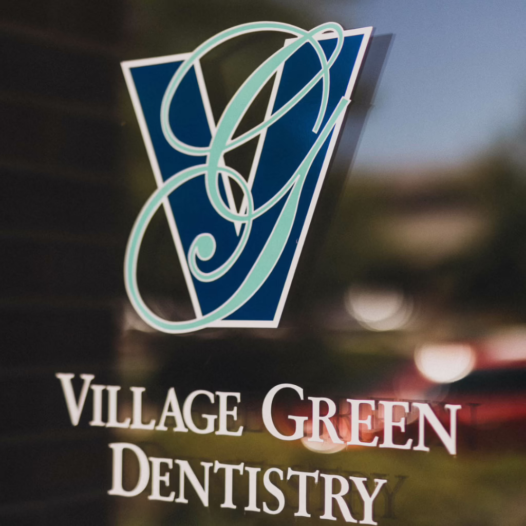 Logo on glass reading Village Green Dentistry with an teal and blue decorative emblem above.